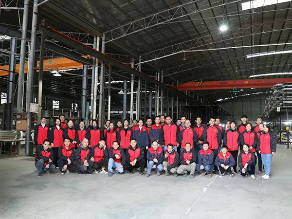 Group of employees in matching red and black jackets posing for a photo inside an industrial factory.
