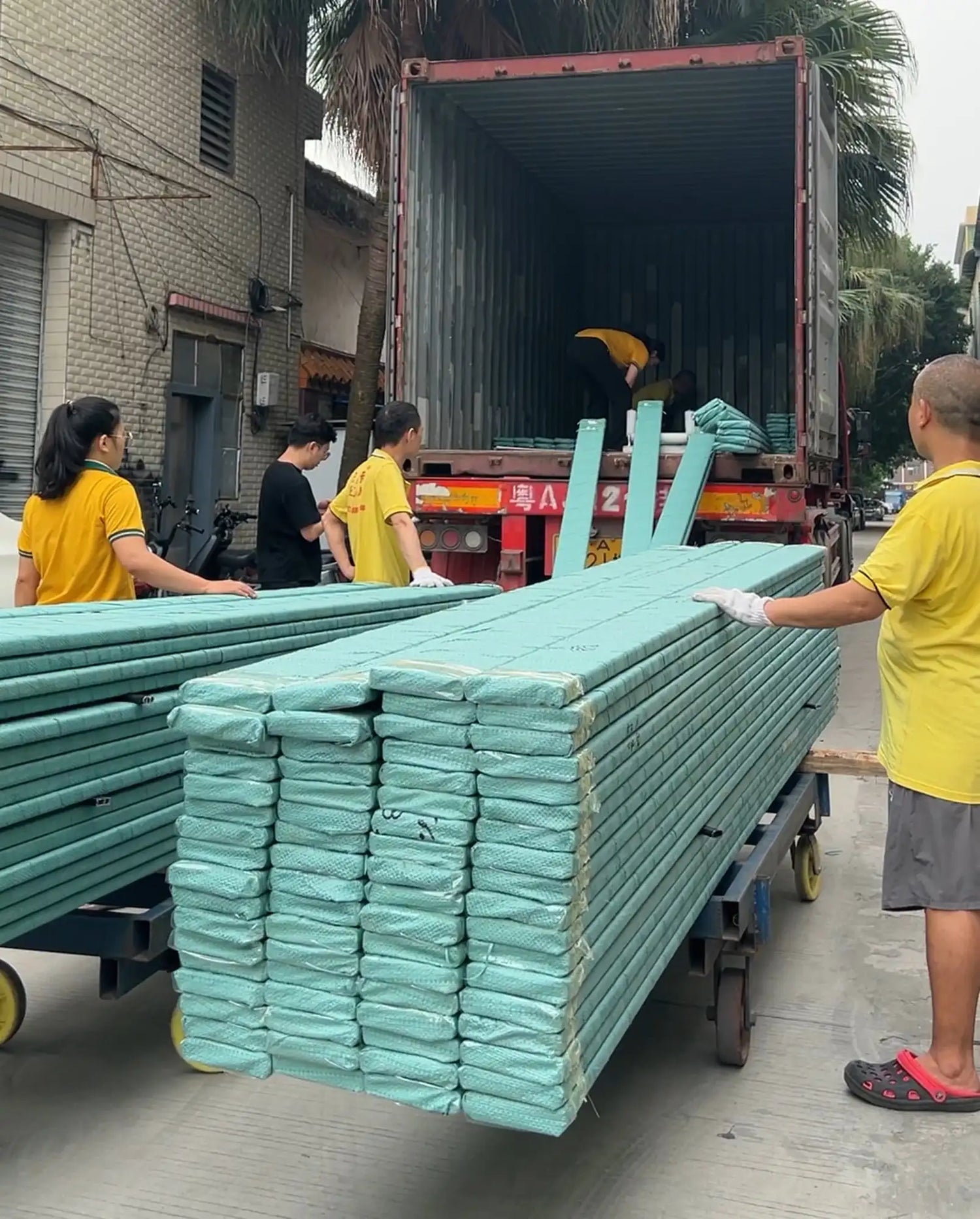 Stacks of light teal-colored, wrapped plastic pipes being loaded onto a truck.